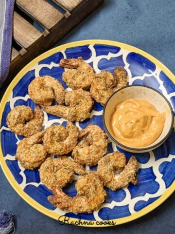 Tasty air fried coconut shrimp with a chilli mayo dip served on a blue plate.