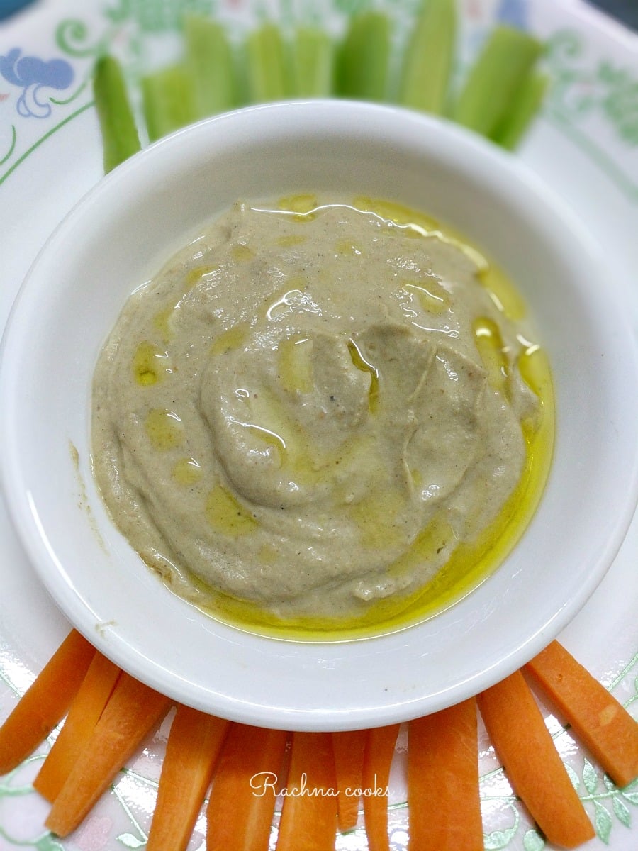 Baba ganoush dip in a white bowl with slices of carrot and cucumber