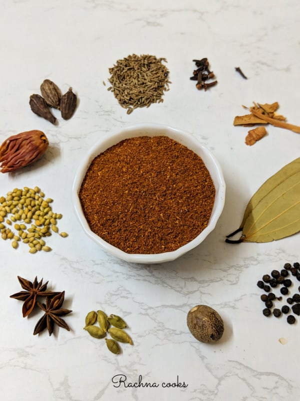 garam masala powder in a bowl surrounded by whole spices.