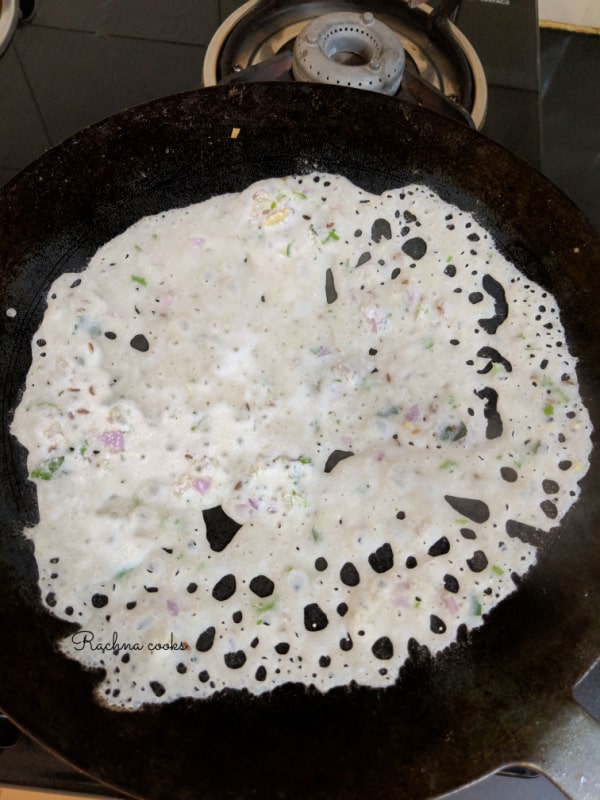 rava dosa spread out on a skillet ready for cooking.