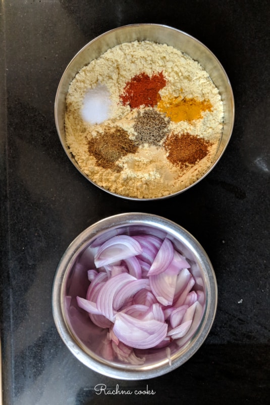 A shallow bowl with chickpea flour, rice flour, spice powders and salt. Along with a bowl of sliced onions.