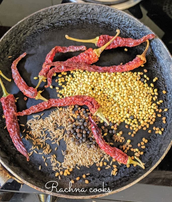 Dry spices coriander seeds, cumin seeds, peppercorn, red chillies and fenugreek seeds being dry roasted on a tawa