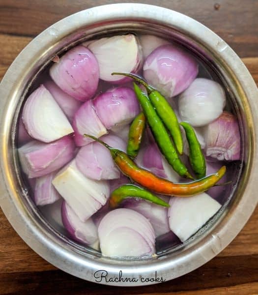 Green chillies and chopped onion covered in water in a shallow utensil.