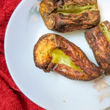 The image shows crispy skin air fryer baked potatoes with centre split and with butter on a white plate.
