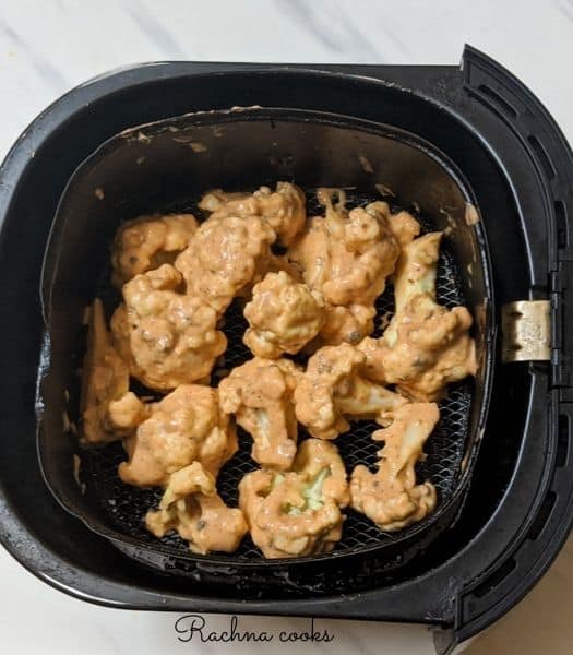 A single layer of coated cauliflower florets in air fryer basket