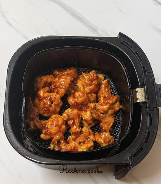 Air fried cauliflower florets in air fryer basket brushed with buffalo sauce