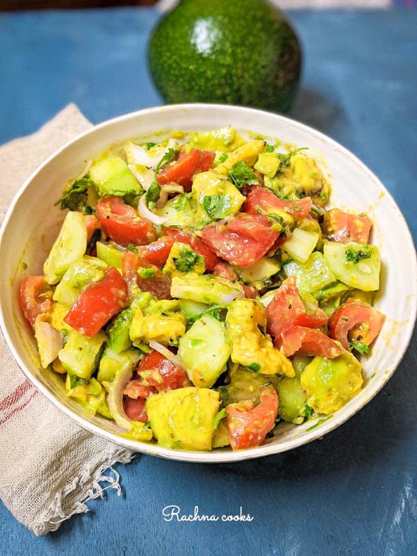large avocado cucumber and tomato salad with onion slices in a white bowl with a blue background