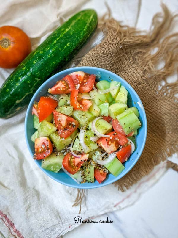 tomato cucumber salad with onion slices in a blue bowl.