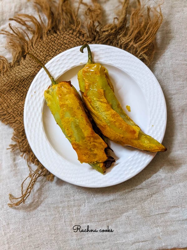 2 Golden mirchi bajjis on a white plate with a brown mat in the background.