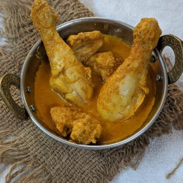 Top shot of half pan with a delicious chicken curry with chicken drumstick and other pieces visible on a brown mat.