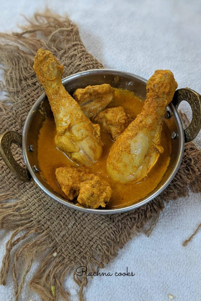 Top shot of a round work/pan with  delicious chicken curry with chicken drumsticks and other pieces visible on a brown mat.