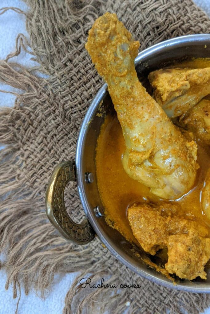 Top shot of half pan with a delicious chicken curry with chicken drumstick and other pieces visible on a brown mat.