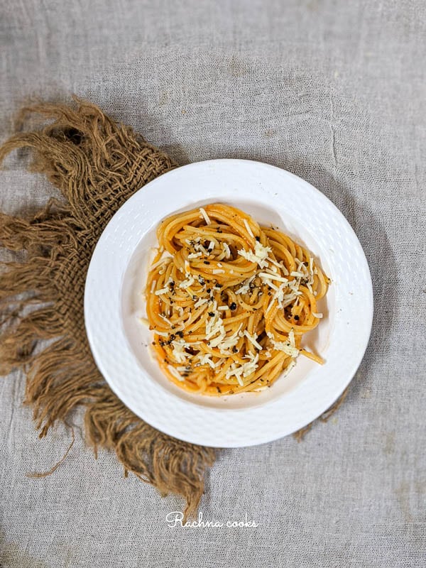 Top shot showing half white plate of pumpkin pasta garnished with cheese and black pepper on a brown mat.