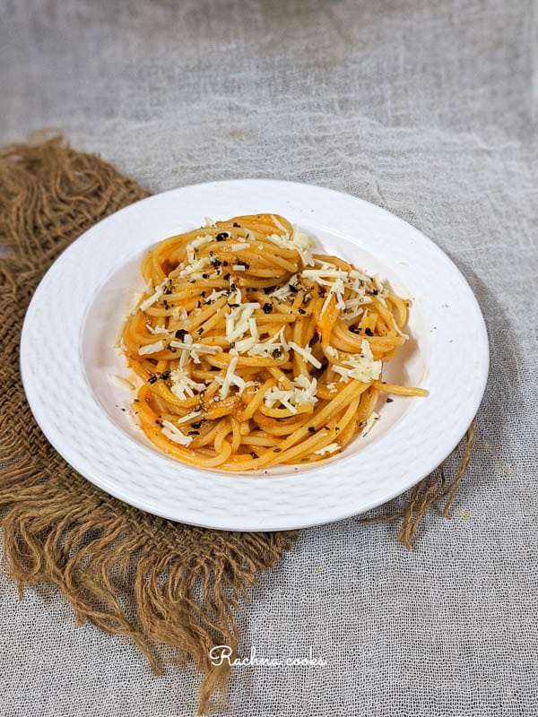 Top shot showing half white plate of pumpkin pasta garnished with cheese and black pepper on a brown mat.