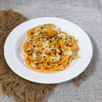 Tasty pumpkin pasta with cheese and pepper garnish on a white plate with a brown mat in the background