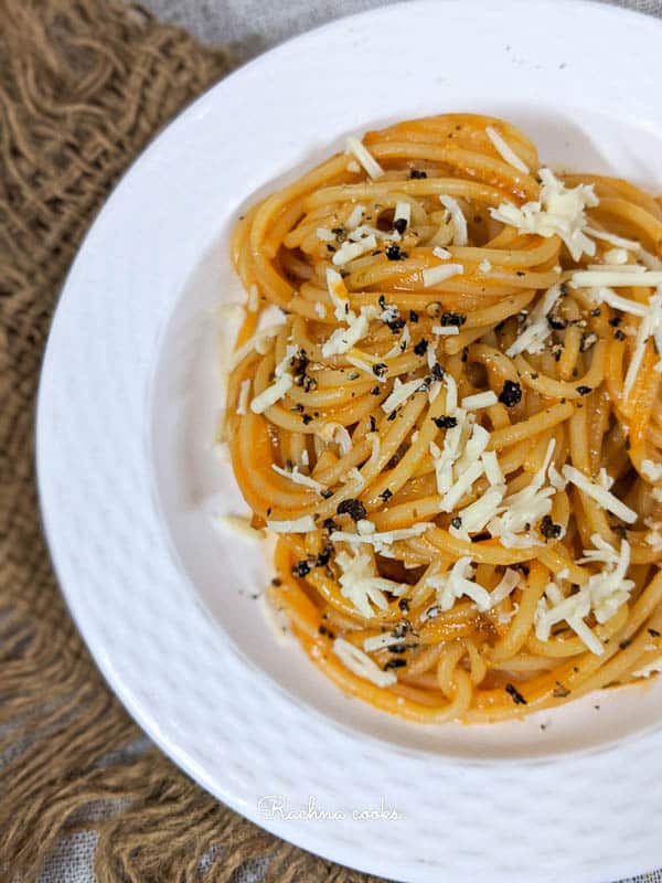 Top shot showing half white plate of pumpkin pasta garnished with cheese and black pepper on a brown mat.