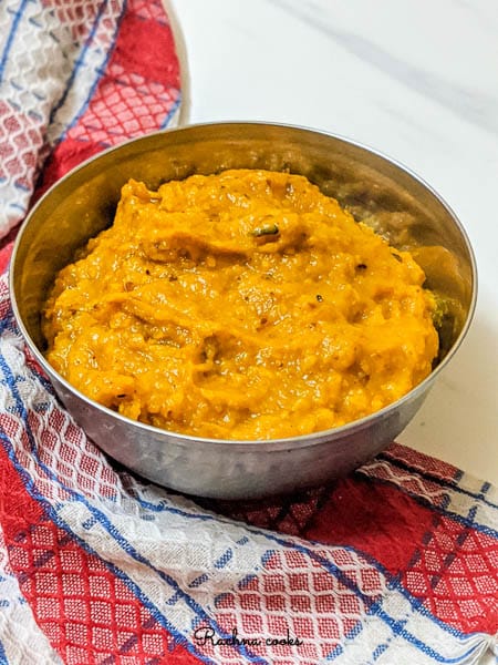 Thick orange pumpkin puree in a bowl with a checked red and white napkin in background.