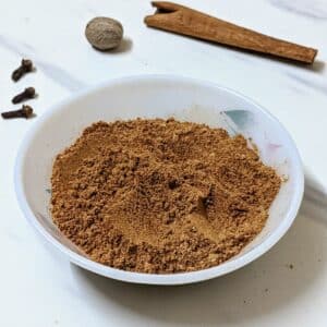 Pumpkin pie spice in a white bowl with a white background and spices in the background.