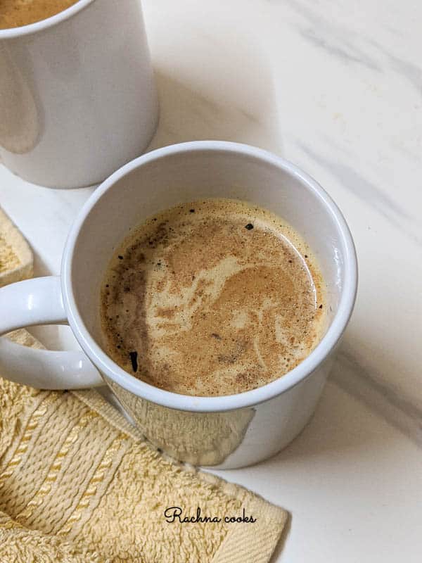 Two white mugs with pumpkin spice latte on a white background with yellow napkin.