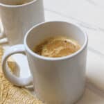 Two white mugs with pumpkin spice latte on a white background with yellow napkin.