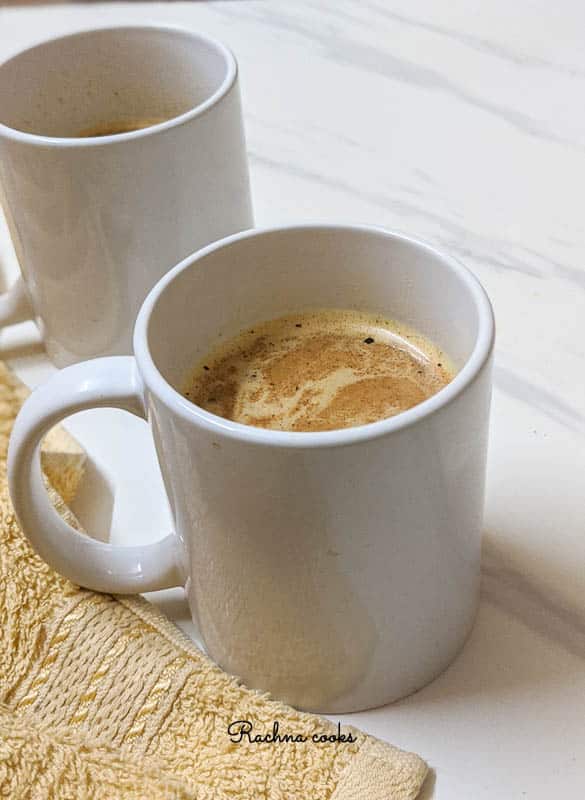 Two white mugs with pumpkin spice latte on a white background with a pale yellow napkin.