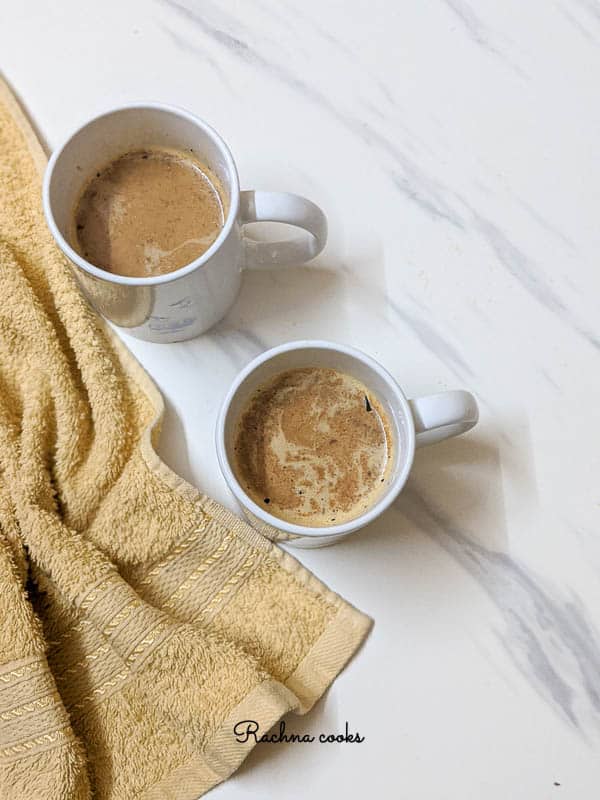 Two white mugs with pumpkin spice latte on a white background with yellow napkin.