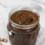 a jar of brown shiny chocolate peanut butter on a white background