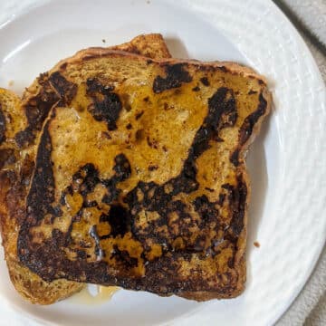 Brown french toast with maple syrup drizzled on top on a white plate