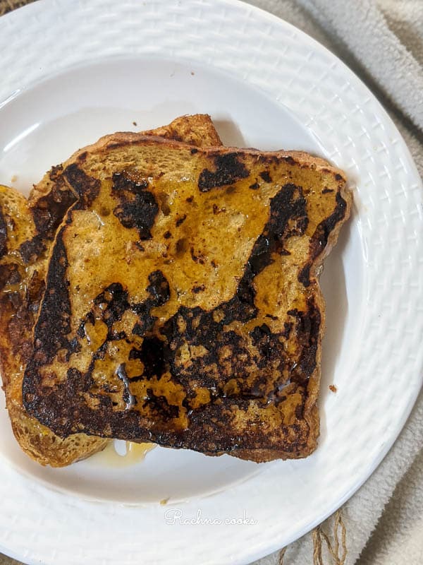 Brown french toast with maple syrup drizzled on top on a white plate