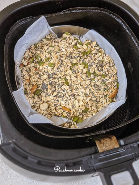 Metal container with parchment lining filled with granola in air fryer basket.