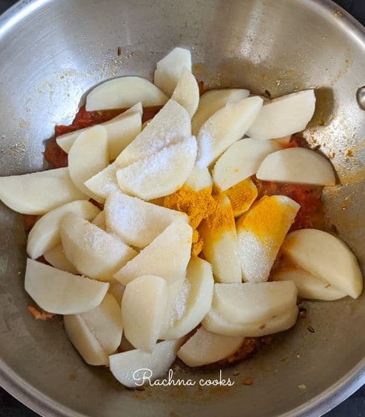 Potatoes added to cooked tomato puree with turmeric powder and salt