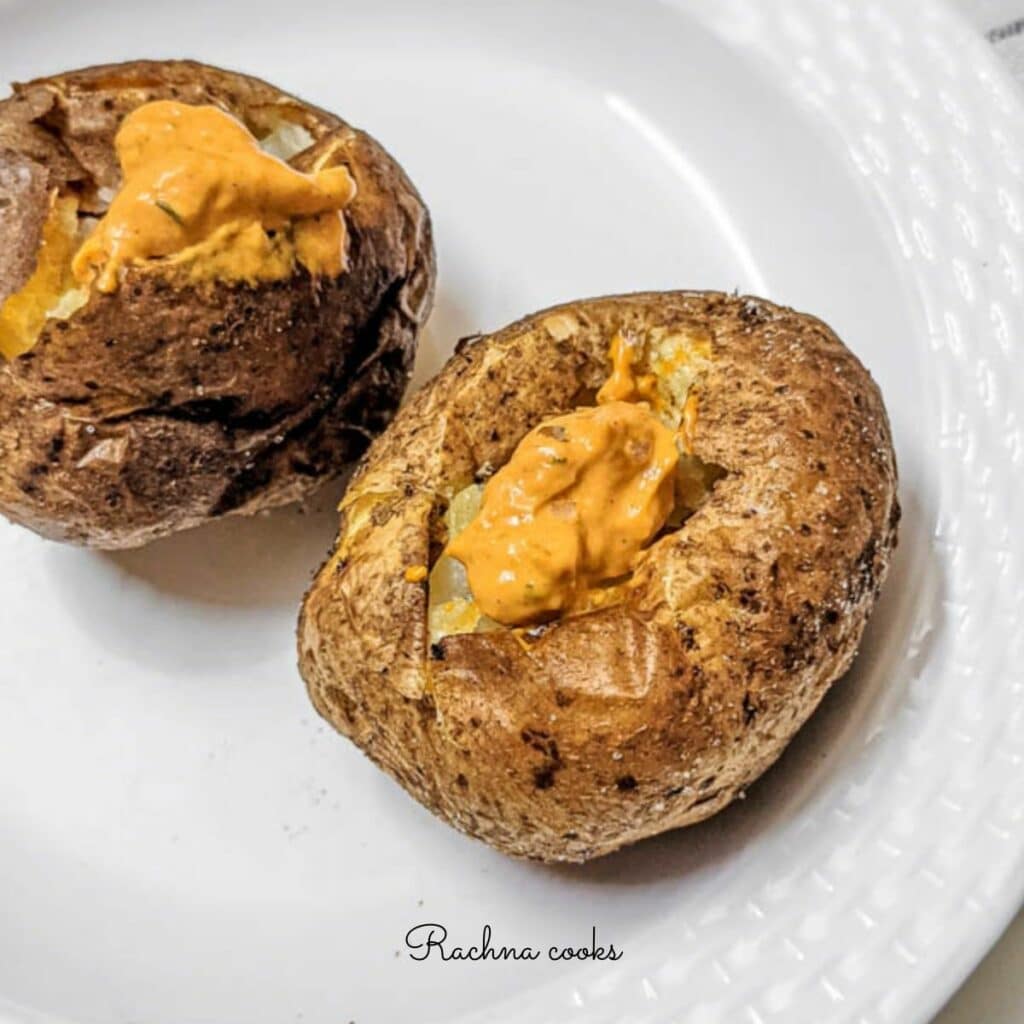 Crispy brown air fryer baked potatoes with a spicy mayo dollop on top on a white background.