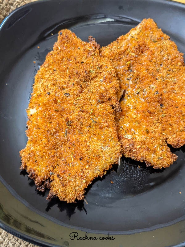 Air fried browned tilapia fillets on a black plate.