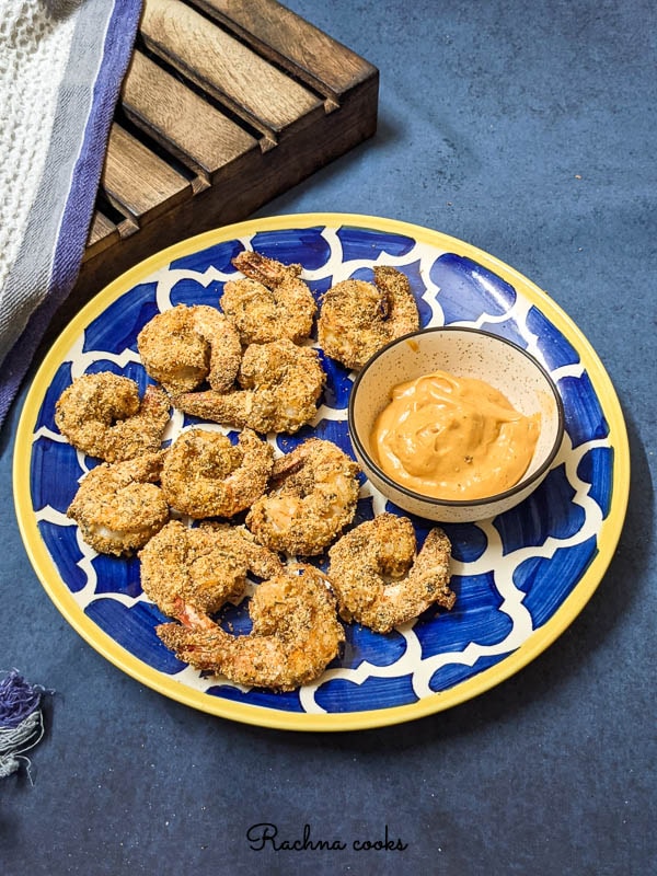 Crispy air fried coconut shrimp on a blue plate with a bowl of chilli mayo dip on a blue background.