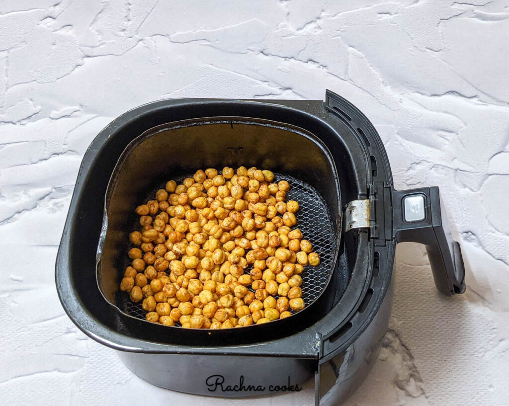 dark chickpeas in air fryer basket after applying spice mix