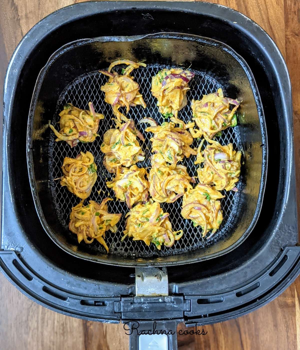 Onion pakoda on the air fryer basket ready for air frying.
