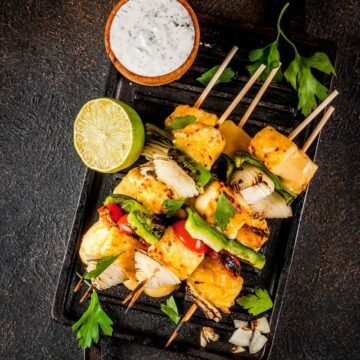 Skewers of paneer tikka with onion and capsicum on a black plate