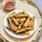 air fried eggplant fries golden on a white plate with ketchup in the background