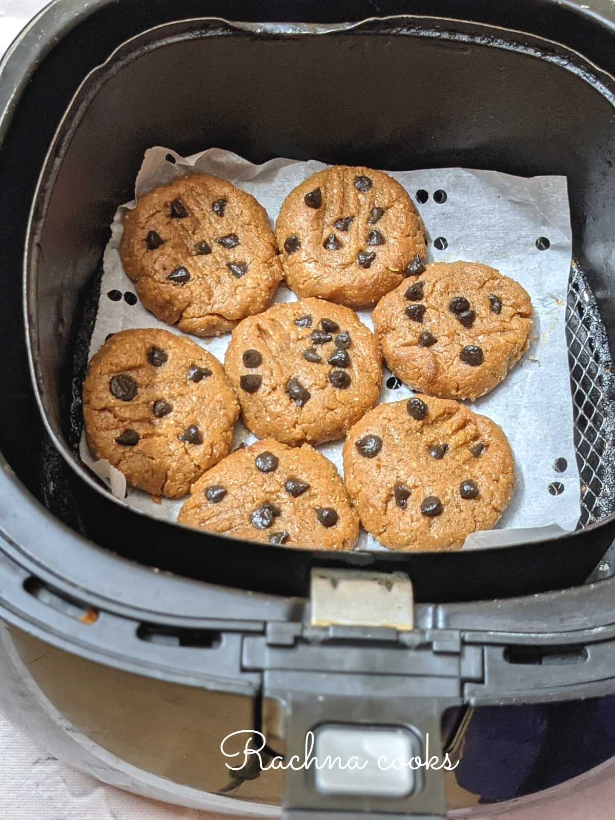 Peanut butter cookies arranged on parchment paper in air fryer basket.