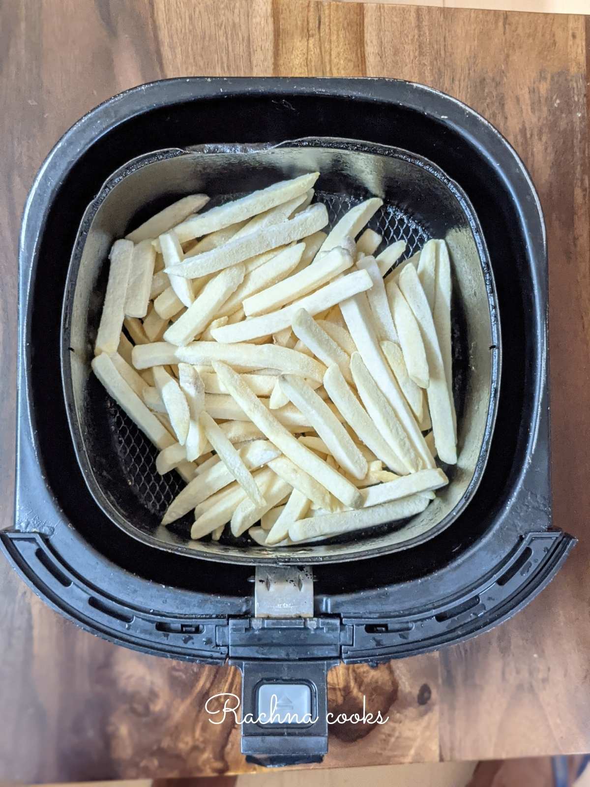 Frozen french fries laid in air fryer basket ready for air frying.