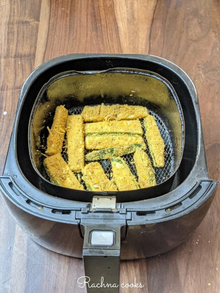 coated zucchini fries kept in air fryer basket for air frying.