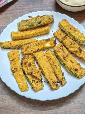 Delicious zucchini sticks with breading served on a white plate.