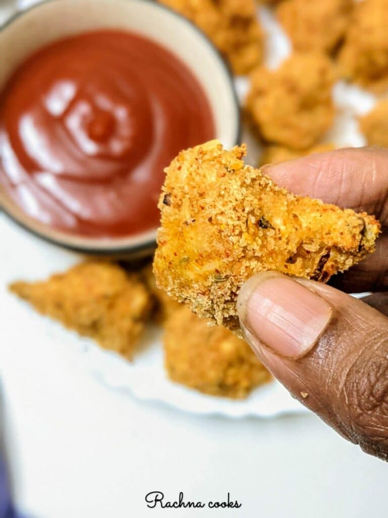 One air fried breaded mushroom held in hand with a ketchup bowl in the background.