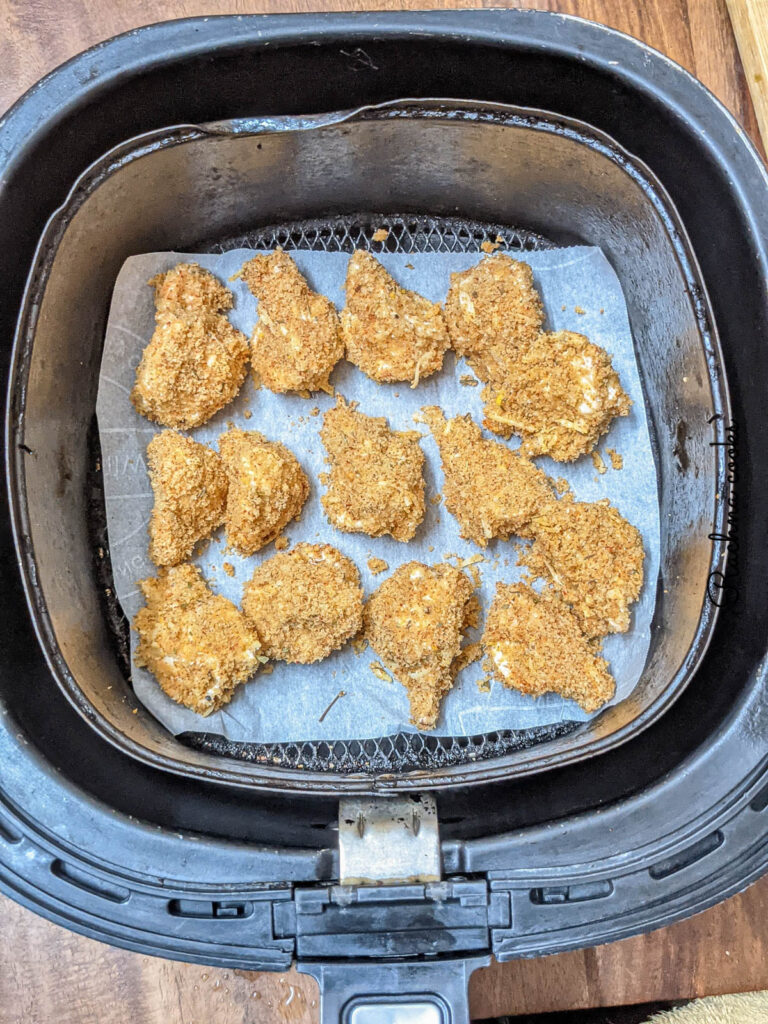 Breaded mushroom on top of parchment paper in air fryer basket.