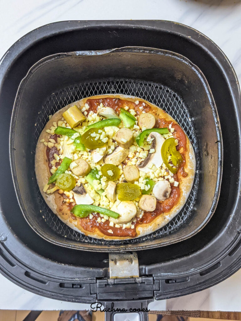 A pizza pie with tomato sauce, cheese and toppings ready for air frying kept in air fryer basket.