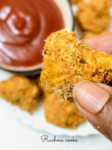 Close up of breaded mushroom air fried held against a bowl of ketchup.