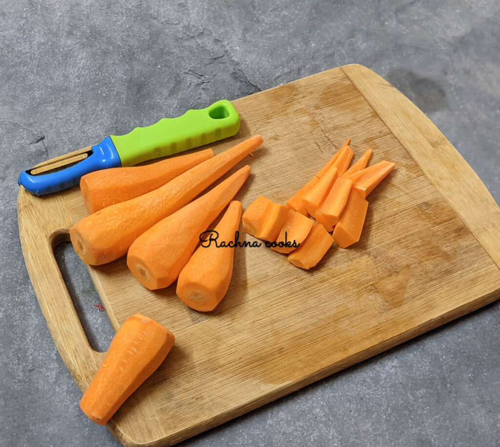 Peeled carrots with one carrot cut into smaller pieces on a brown chopping board.