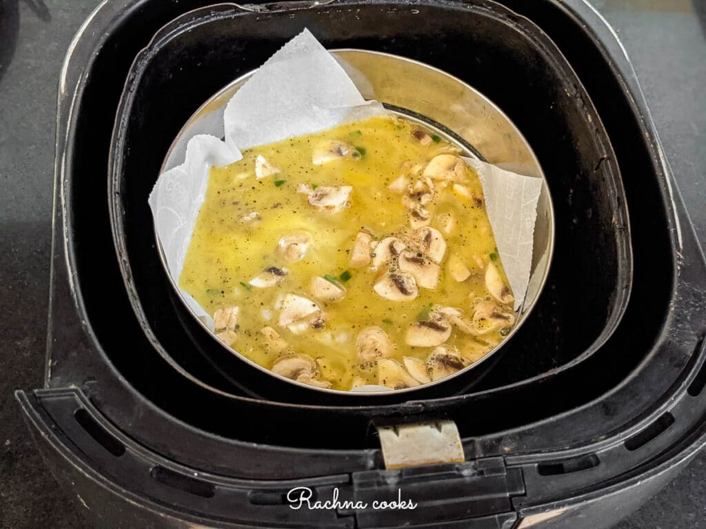 Beaten eggs mixture in a tin with a parchment paper inside air fryer basket.