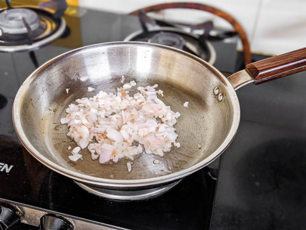 A shallow pan with minced garlic and chopped onion being fried.