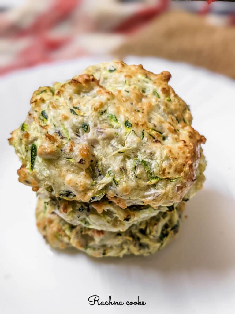 3 air fried zucchini fritters stacked on top of each other on a white plate.